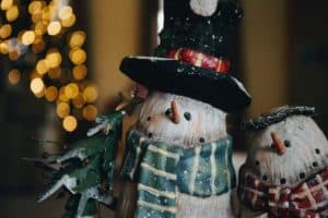 two snowman decorations, one with a top hat and green striped scarf and the other with a flat hat and a red checkered scarf look into the camera