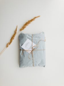 a  blue-gray wrapped package sits on a white surface. Two heads of grain are beside the package. The package is wrapped with beige twine, about the same shade as the grain. 