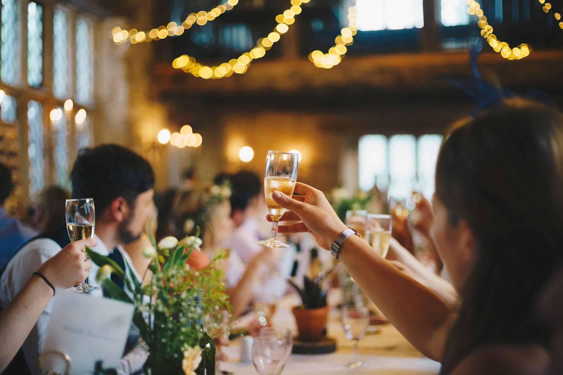 A large formal event. People are gathered at a long wooden table. Everyone is raising a glass for a toast