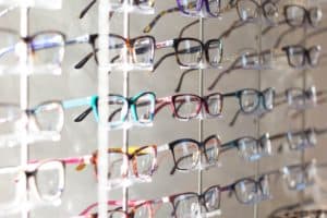 A glasses display in a sales location.  There are many types of glasses against the wall, hung in orderly columns.  