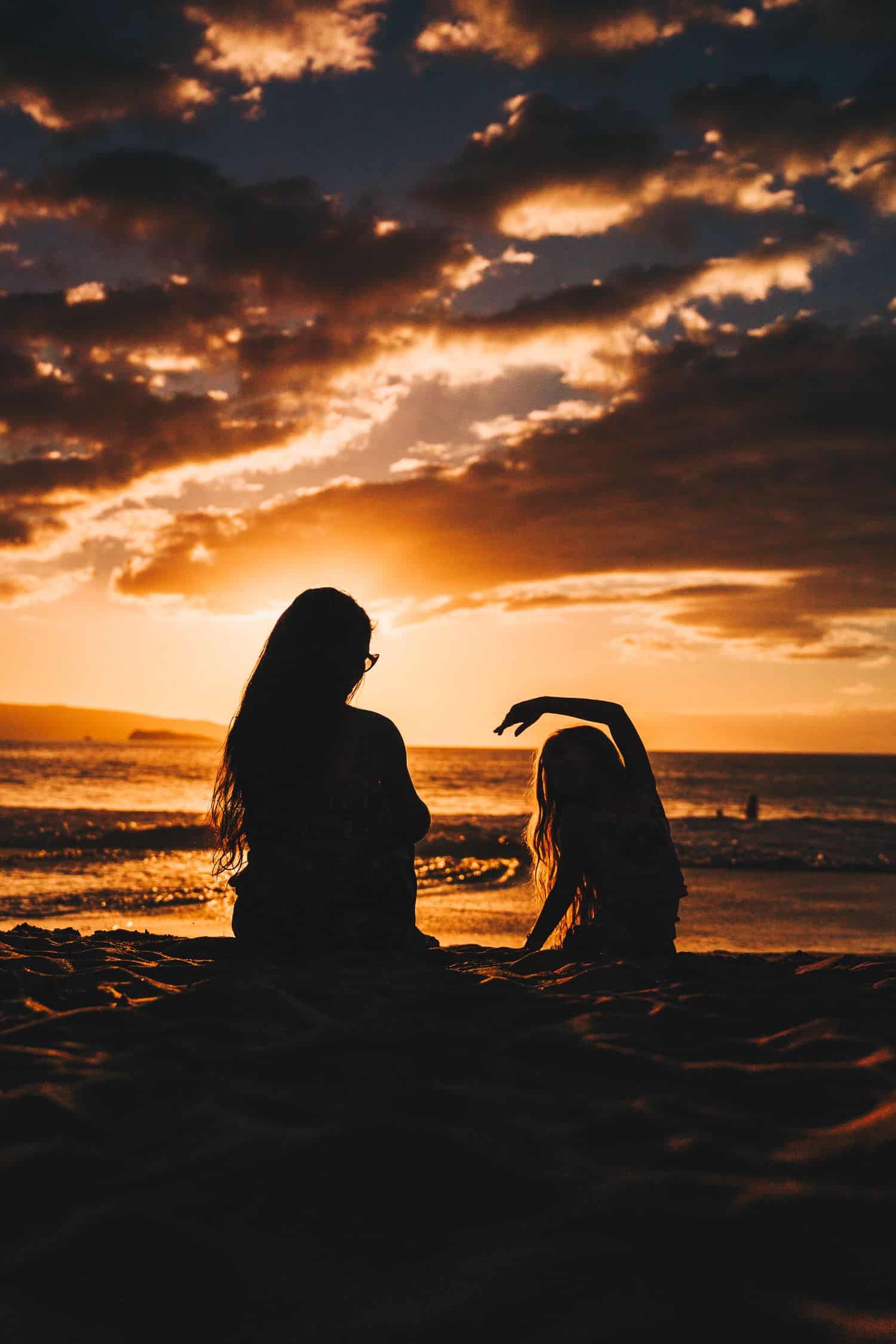 shadowed image of a woman and her daughter sitting on the beach together