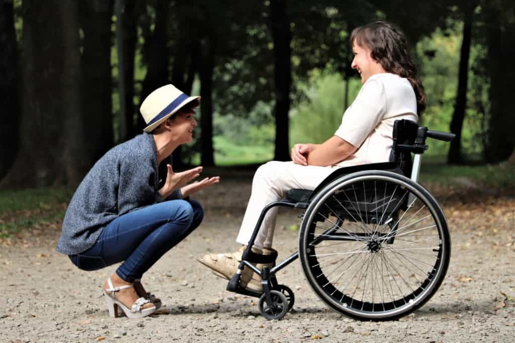 woman in wheelchair talking with another woman crouched in front of her