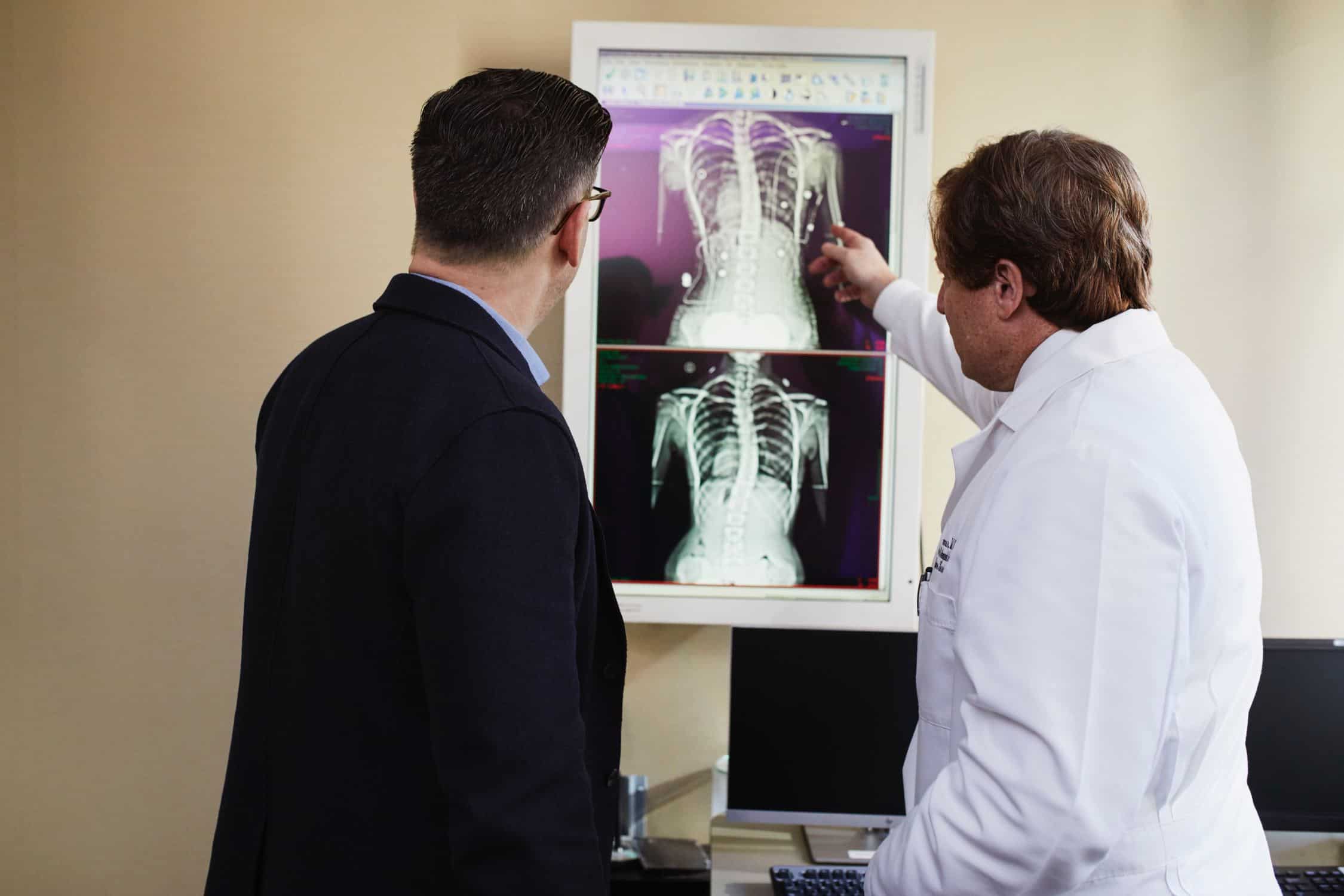 a doctor and patient, both white men look at a series of CAT scans on a light board. The doctor is gesturing at one of the images.