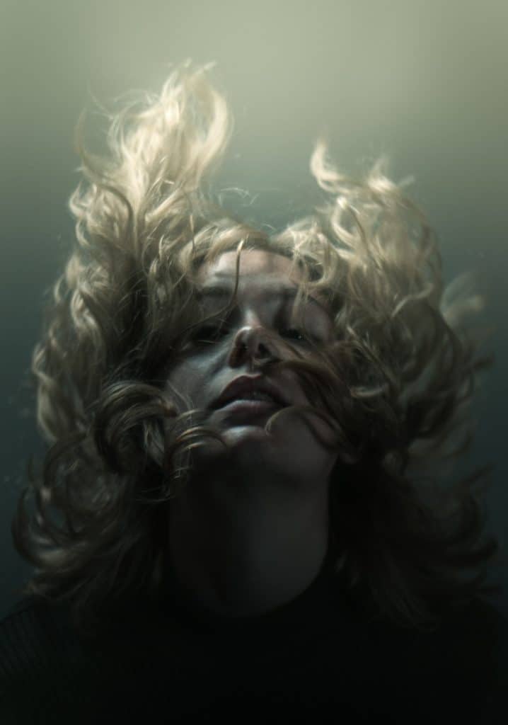 woman underwater in murky surroundings, eyes closed and hair floating upward