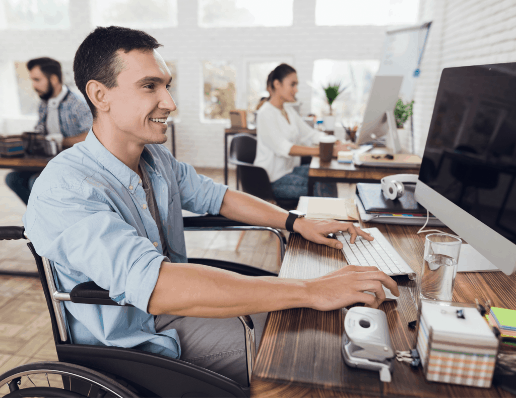 white man in wheelchair and business suit, working in an open office space at a computer
