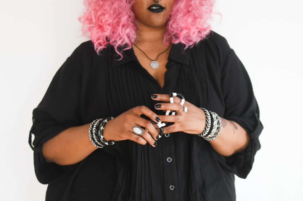 Close-up of a Black and Indigenous austistic non-binary person with pink ombré hair, black lipstick, black nail polish, tattoos, and bracelets using a tangle stim toy.