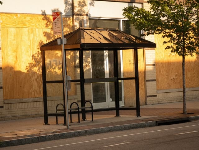 A bus shelter at the side of a road, with a brick building visible behind it.