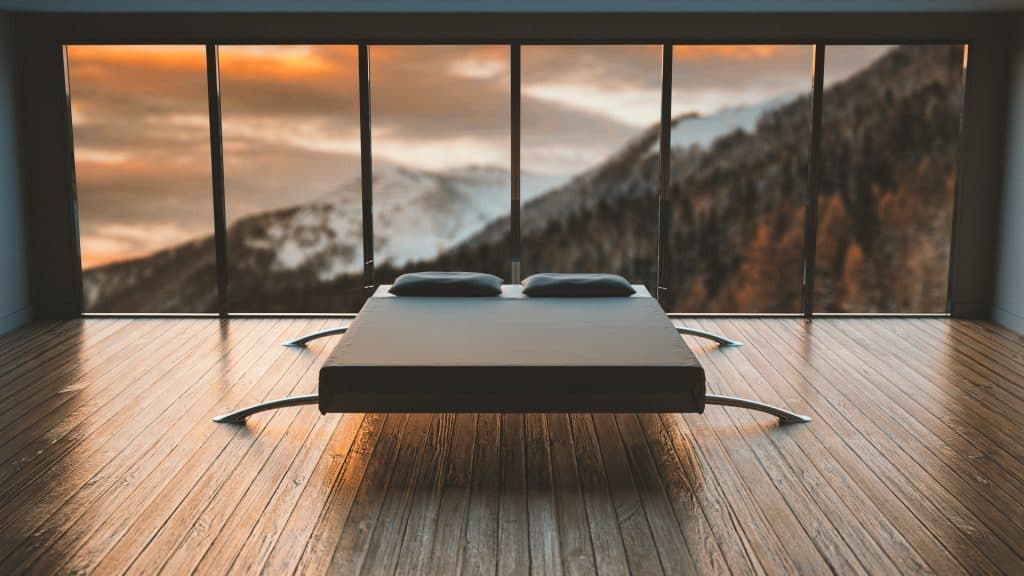 black mattress above a wooden floor in a room with a wall-length picture window displaying a mountain at sunset.